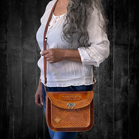 Model displaying brown Cuyuni bag  hanging from a single strap on her shoulder. Bag features an intricate design and a flap closure. Made by Gy Crafts.