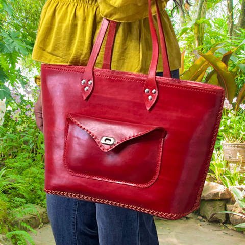 Model displaying red Kimbia tote bag hanging from her shoulder, made from Argentinian leather featuring an exterior pocket and two straps. Made by Gy Crafts.