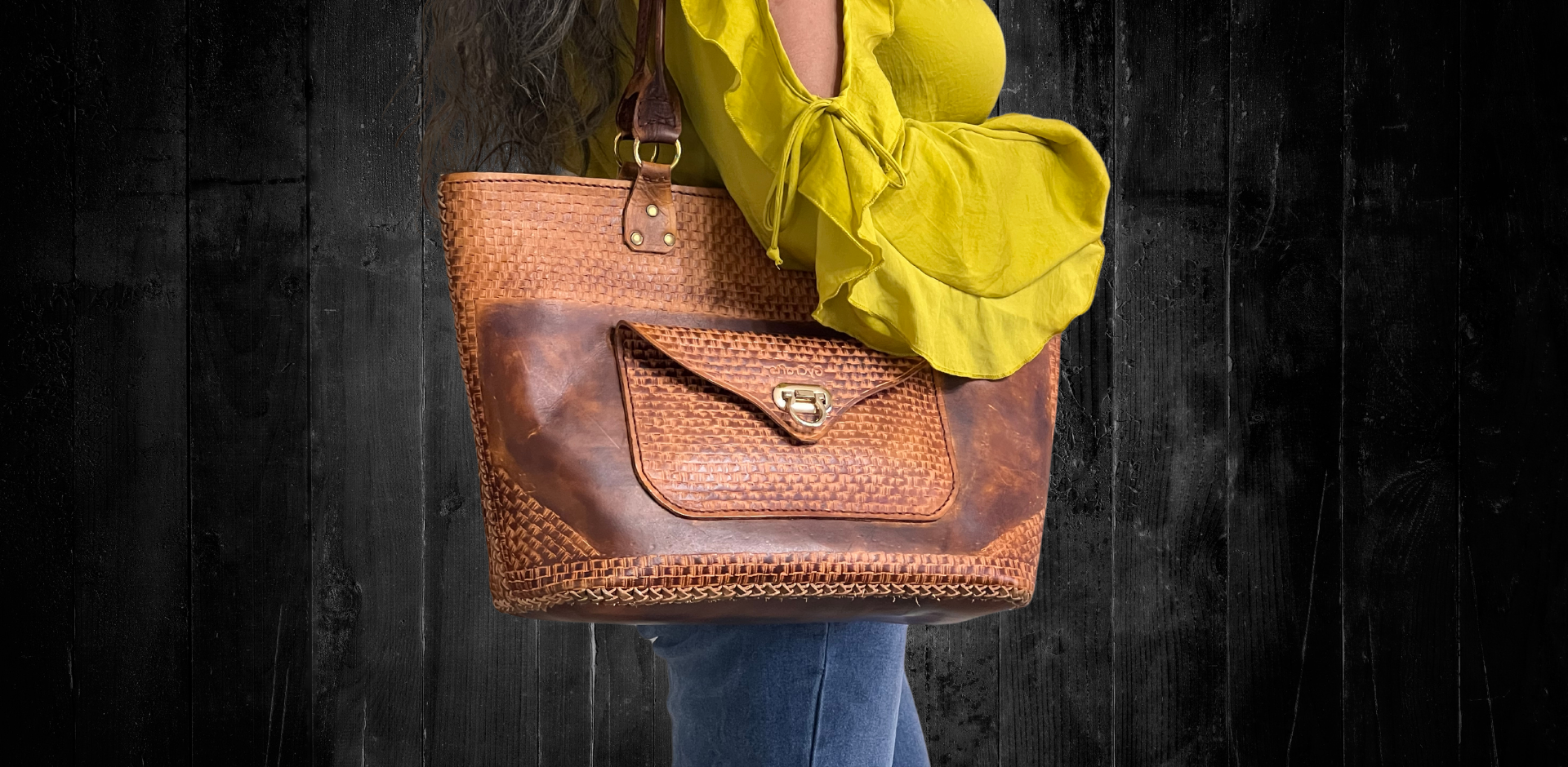 Model displaying brown kimbia bag hanging from her shoulder featuring outer pocket with flap closure. Made by Gy Crafts