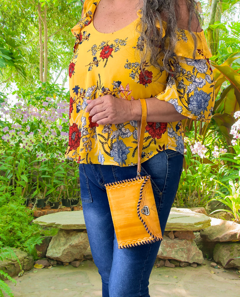 Model displaying yellow Ituni wristlet hanging from her hand closer to her wrist. Bag has a flap closure